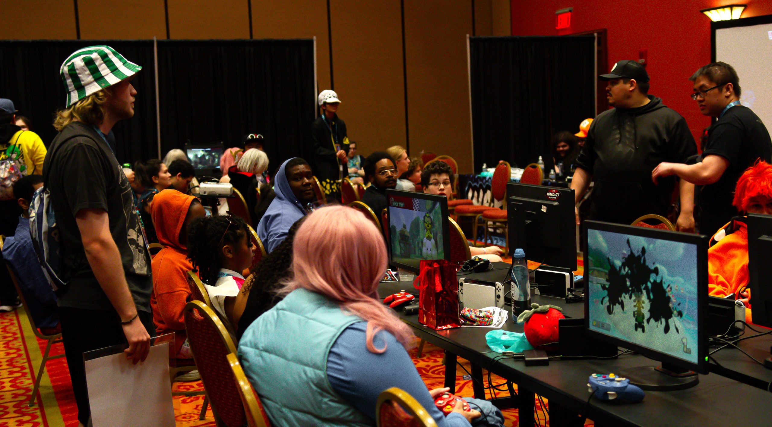 A group of gamers are seat at consoles in front of games, participating in a video game tournament at Soonercon.